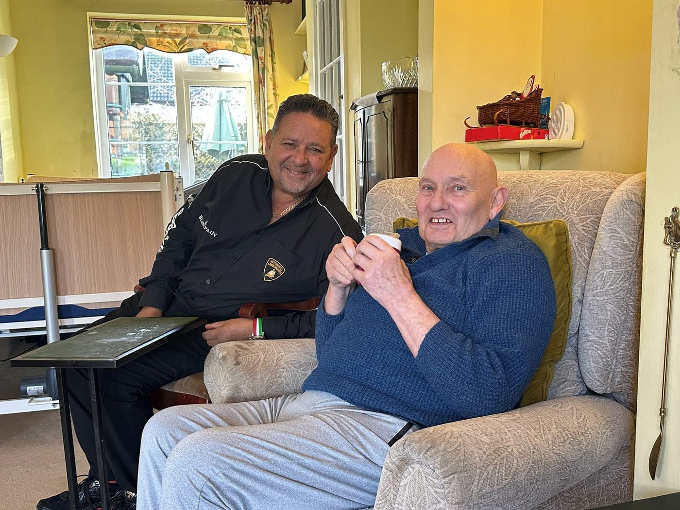 The client sitting at home with a cup of tea, alongside the friend who brought the Lamborghini